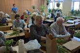 Seniorzy obwijają mchem korzenie rośliny i ziemię, następnie związują sznurkiem tworząc kokedamę.