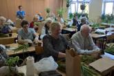 Seniorzy obwijają mchem korzenie rośliny i ziemię, następnie związują sznurkiem tworząc kokedamę.